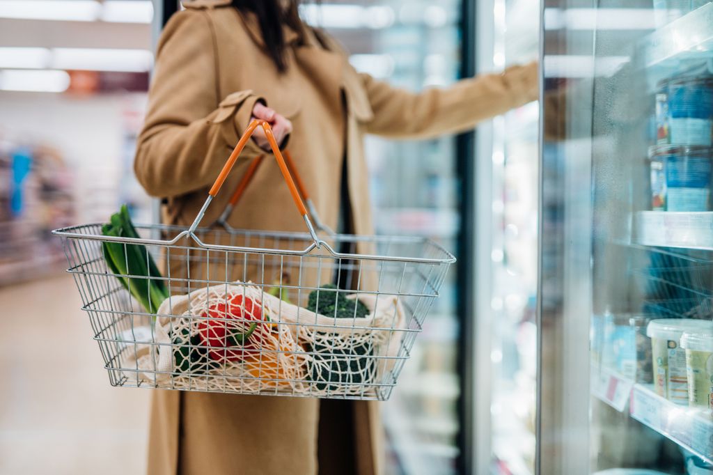 Close up shot of woman carrying shopping basket and shopping groceries in supermarket. City solo life concept. Single person.