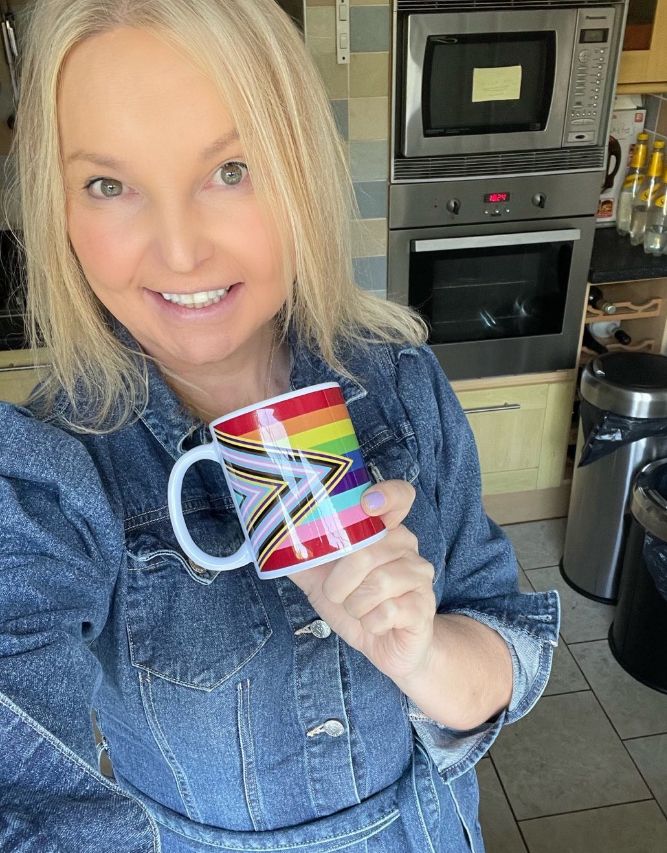 India Willoughby in a kitchen holding a mug with a rainbow design