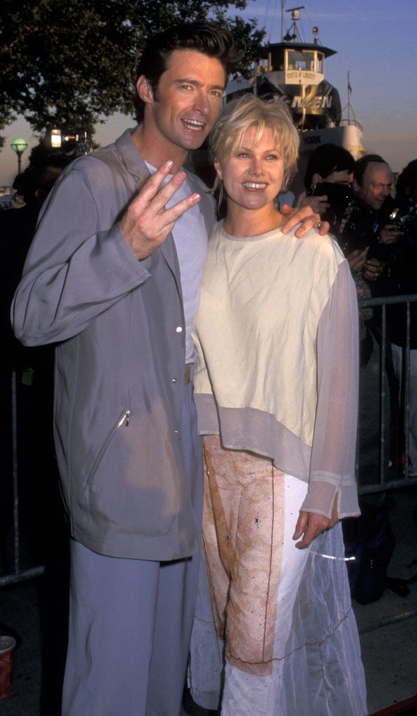 Hugh Jackman holding three fingers up next to wife Deborra-Lee in a blue outfit