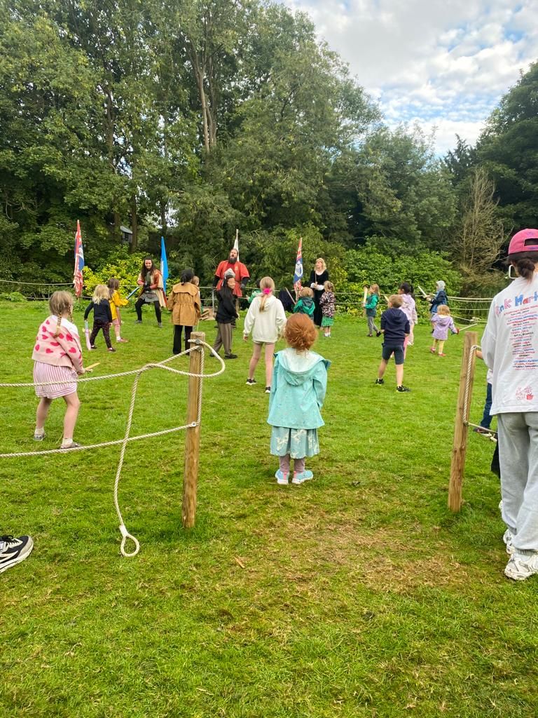 Children standing in a field holding pretend swords learning to be knights.
