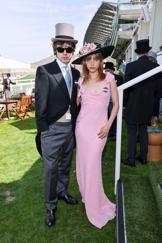 Lennon Gallagher and Isobel Richmond at Royal Ascot pose in modern formalwear; she wears a pink Self Portrait slip dress and black hat, he wears top hat and sunglasses.