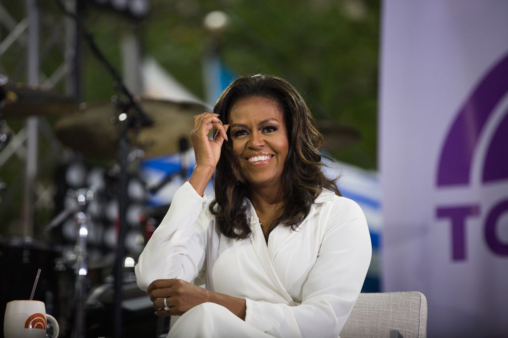 Michelle Obama smiles while wearing a white suit