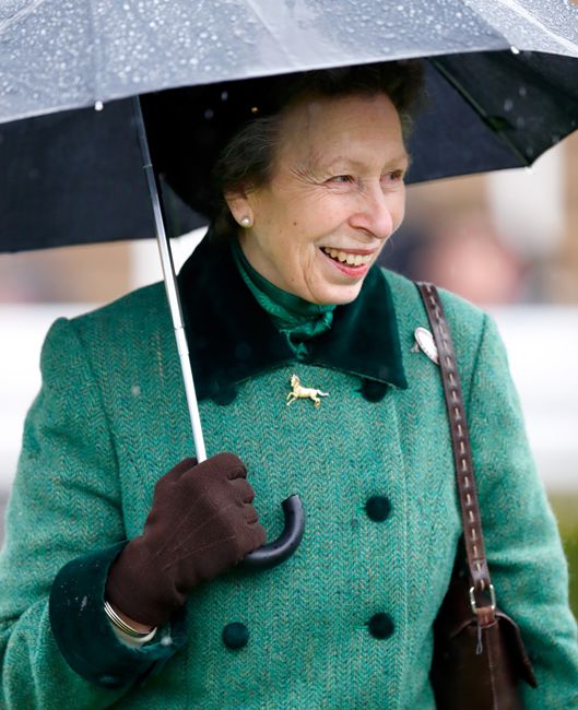 princess anne in green coat smiling as she holds umbrella