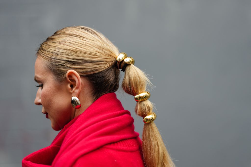 A guest wears a red scarf, red wool top, golden jewelry as attachments for the ponytail, earrings, outside Brandon Maxwell, 
