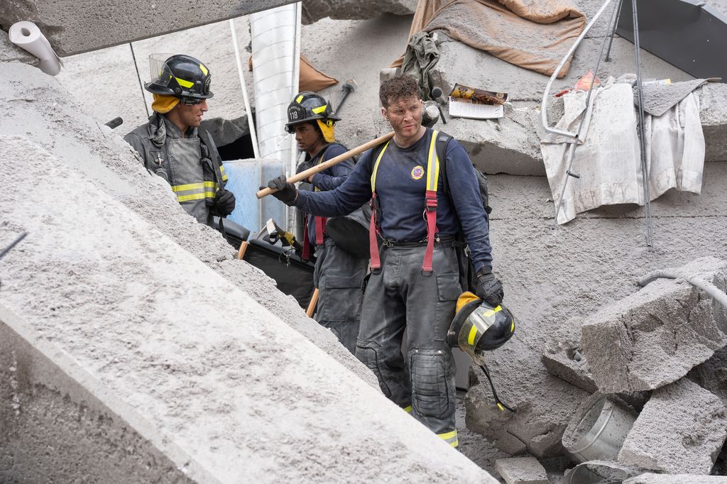 A collapsed high-rise apartment building with firefighters in the rubble 