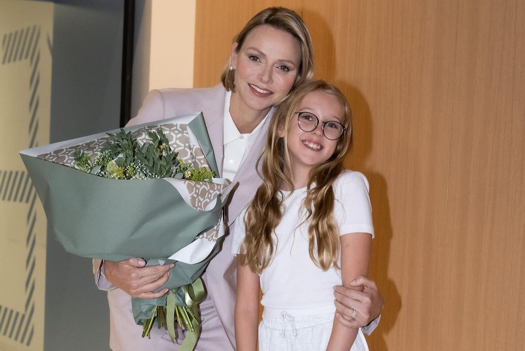 Princesa Charlene sorrindo segurando flores com uma jovem