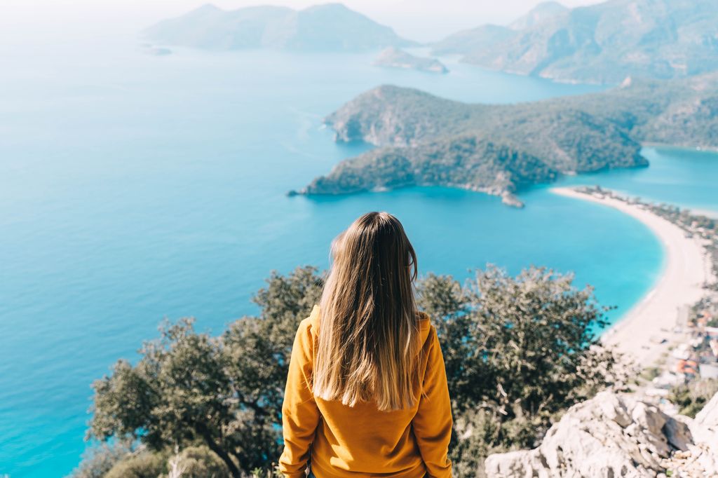 Young woman travels in the mountains, a beautiful view around. Turquoise sea and islands on background. Rear view.