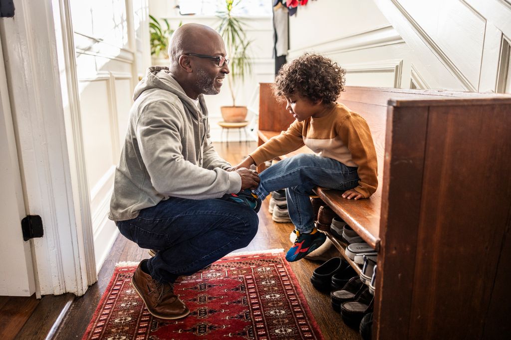 Father tying toddler boy's shoes in hallway