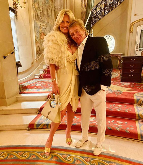 penny lancaster in white dress and fluffy stole posing with husband rod stewart