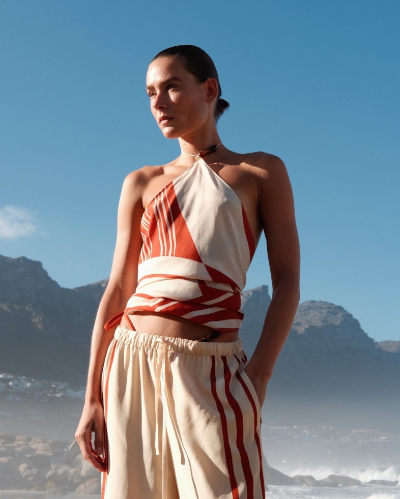 model in orange-cream halterneck top by a beach
