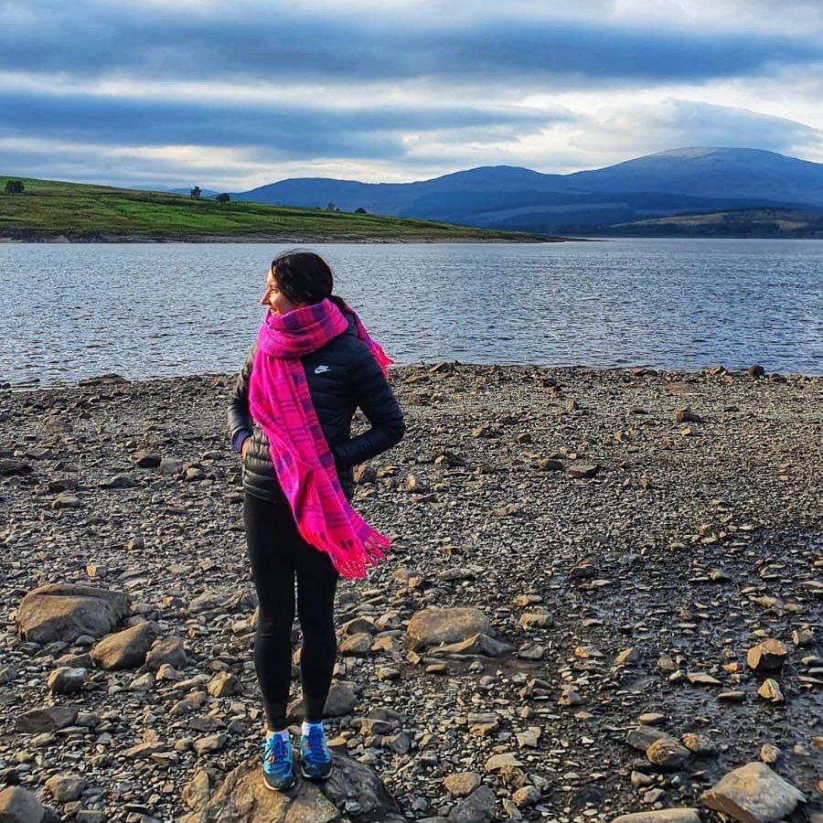 Young woman in front of a loch in a pink scarf