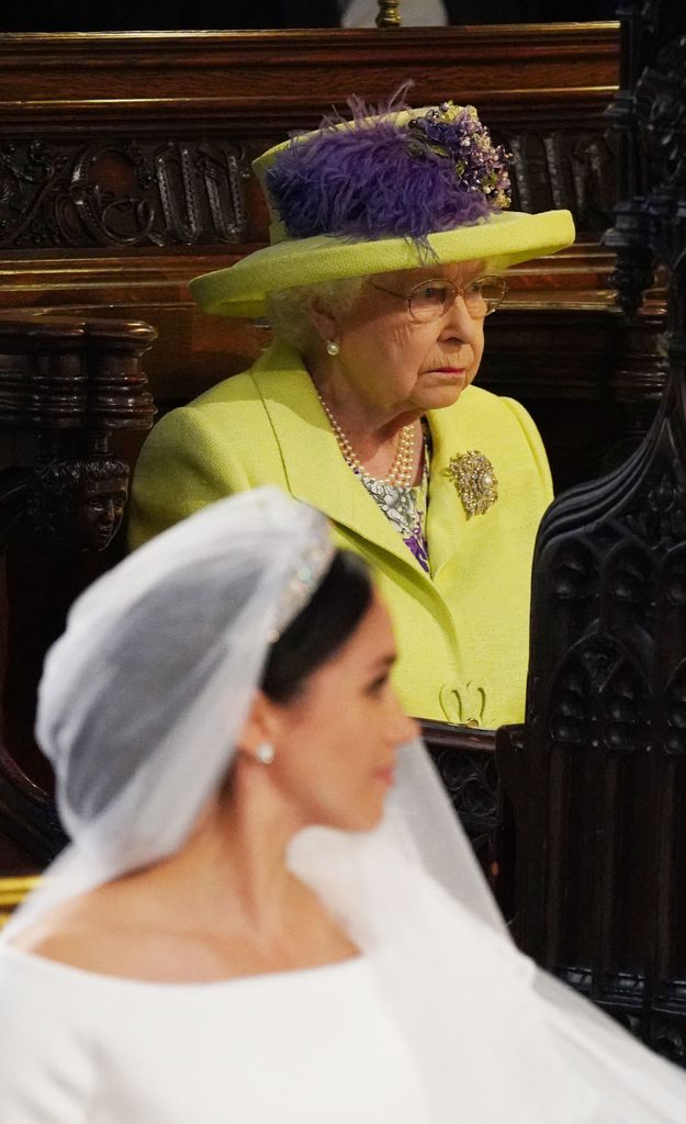 Queen Elizabeth II with a straight face behind bride Meghan Markle