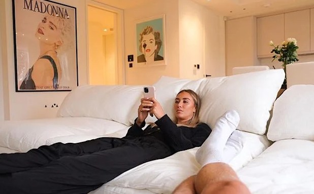 Sophie Habboo regardant son téléphone en allongeant sur son canapé blanc dans l'appartement de Londres