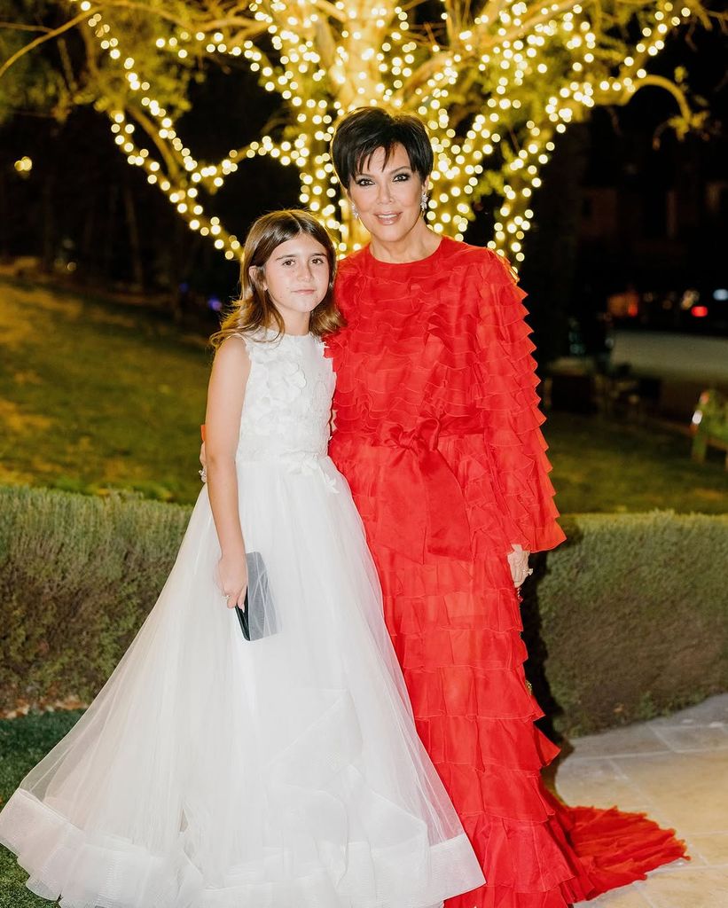 Kourtney Kardashian's daughter Penelope in a white chiffon gown poses with Kris Jenner in a red chiffon gown