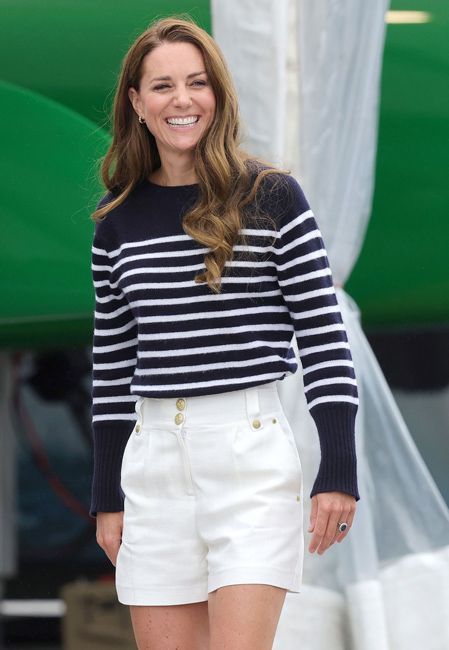 kate smiles as she walks outside in white shorts that are decorated with gold buttons and she also wears a navy and white stiped top