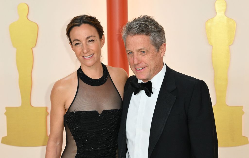 Anna Eberstein dalam gaun hitam dan Hugh Grant dalam tuksedo hitam