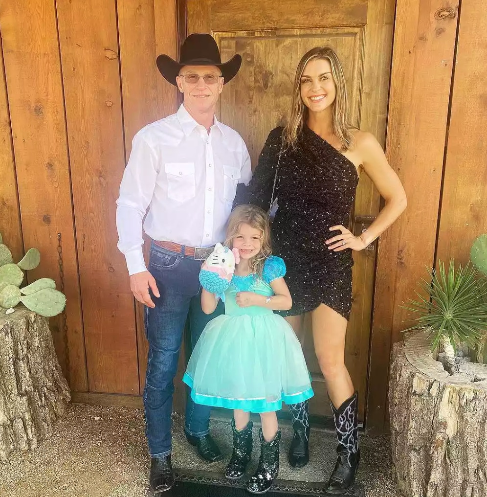 Ty in white shirt and cowboy hat with his wife in black dress and daughter in blue princess dress