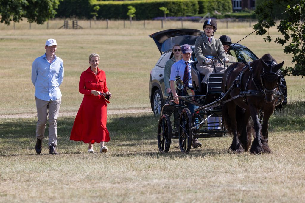 Lady Louise Windsor in carriage with mum Sophie in red dress on foot beside felix da silva clamp
