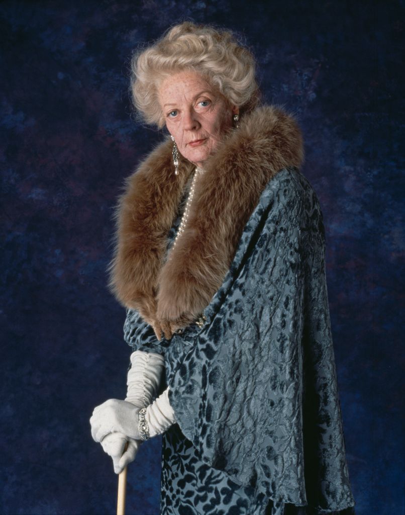 British actress Maggie Smith on the set of Spielberg's film Hook, Maggie Smith stands dressed in an opulent, old-fashioned outfit with a fur collar draped around her neck. 