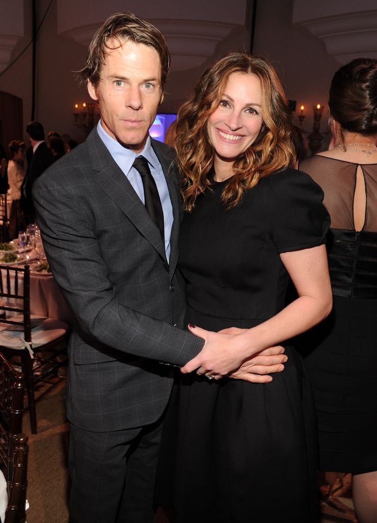 Julia Roberts smiling wear a black dress with her arms around Danny Moder
