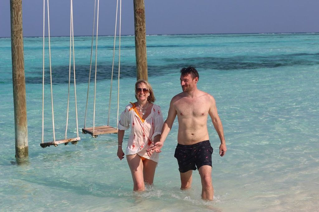 Carol McGiffin in a white cover up holding hands with her husband in the sea