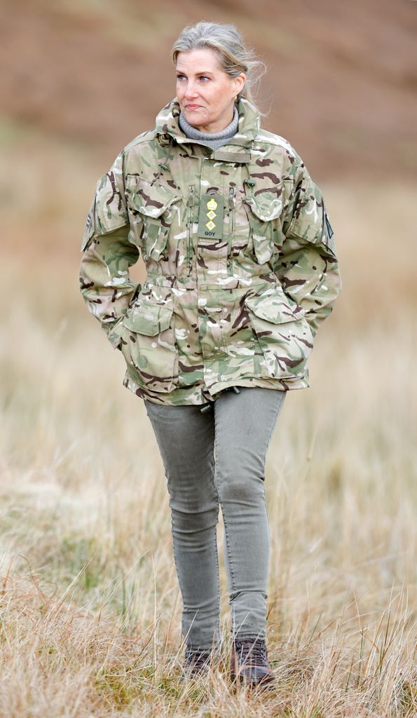 Sophie, the Duchess of Edinburgh walks through grass wearing a camo jacket and jeans