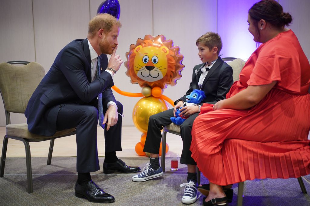 Prince Harry sitting in a chair talking to a boy and his mum at wellchild