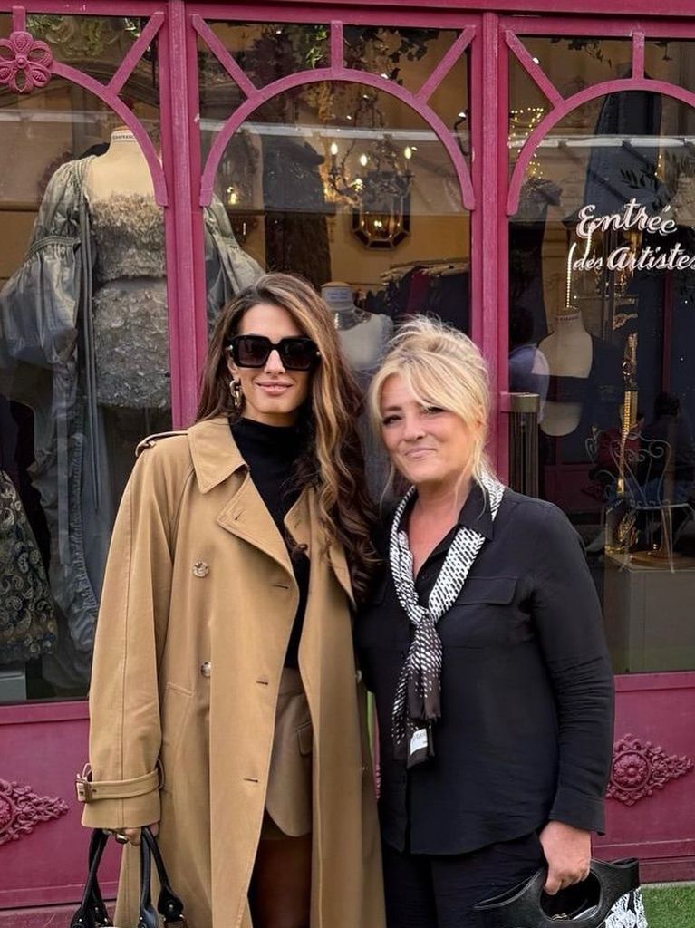 Amal in tan trench coat beside woman outside shop