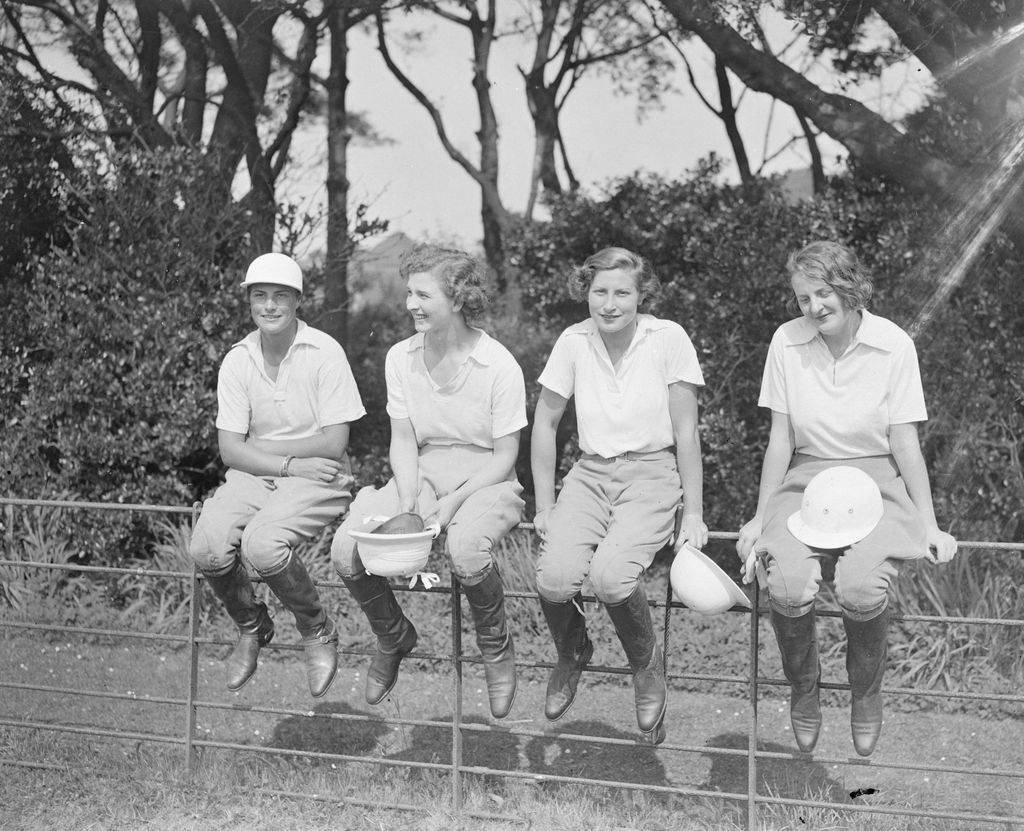 Black-and-white image of four ladies sitting on a fence