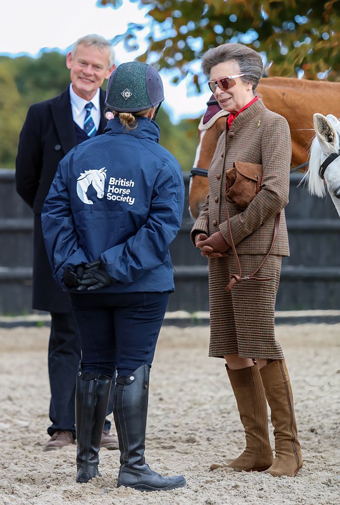 Princess Anne standing with Martin Clunes and a horse and rider at Bovington Equestrian Centre
