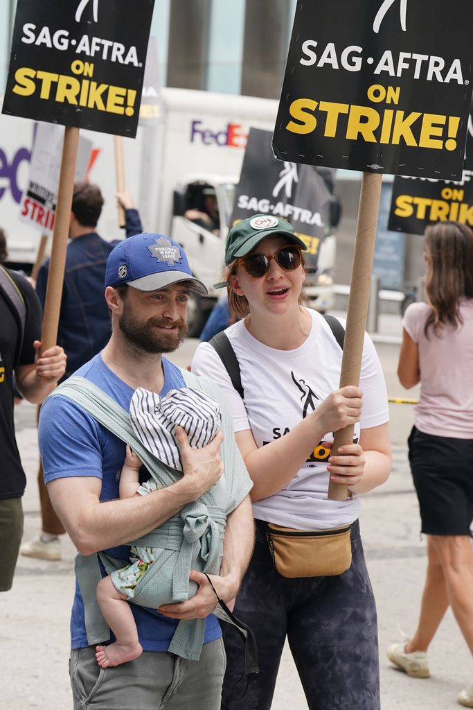 Daniel Radcliffe carrying baby boy with Erin Darke holding sign