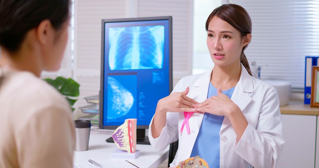 doctor wearing white coat with pink ribbon explaining breast self-examination to woman 