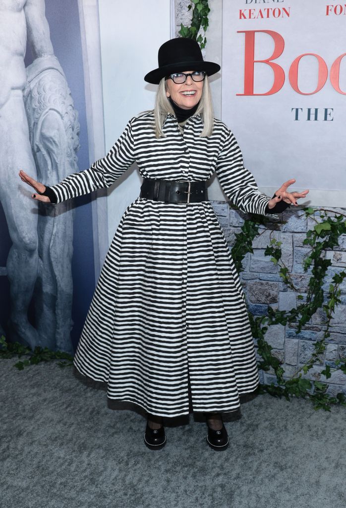 Diane Keaton souriant dans une robe rayée en noir et blanc avec un chapeau