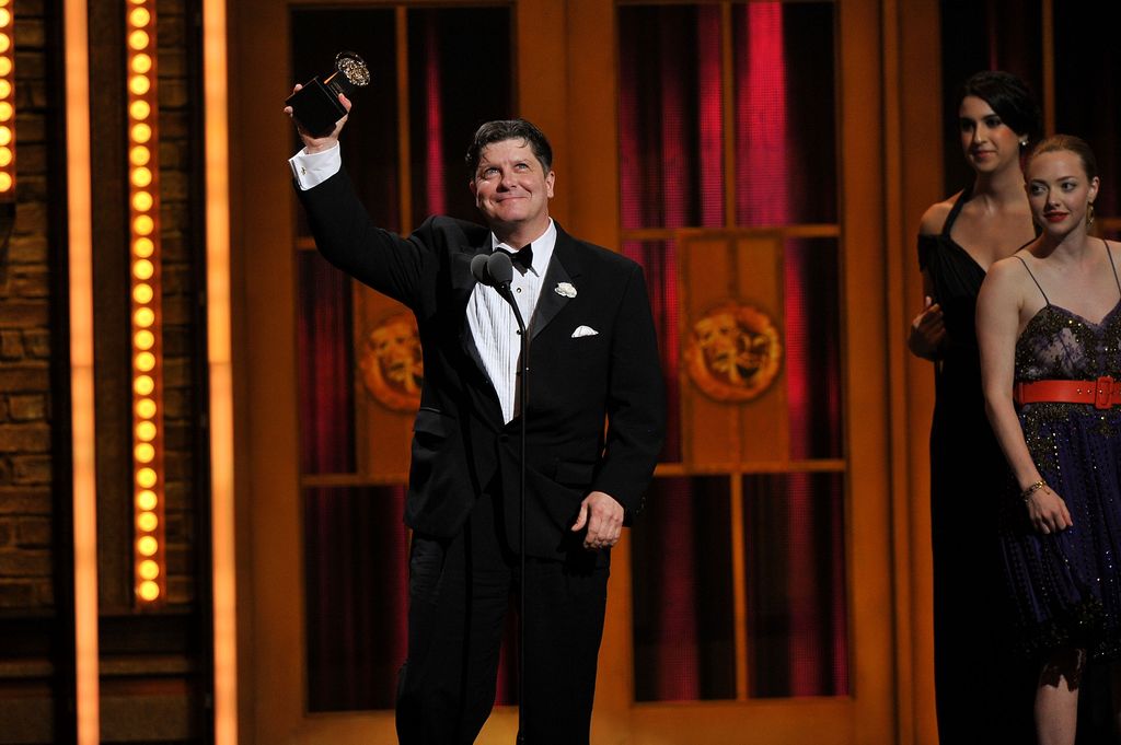 Michael McGrath holds up his Tony Award on stage after winning