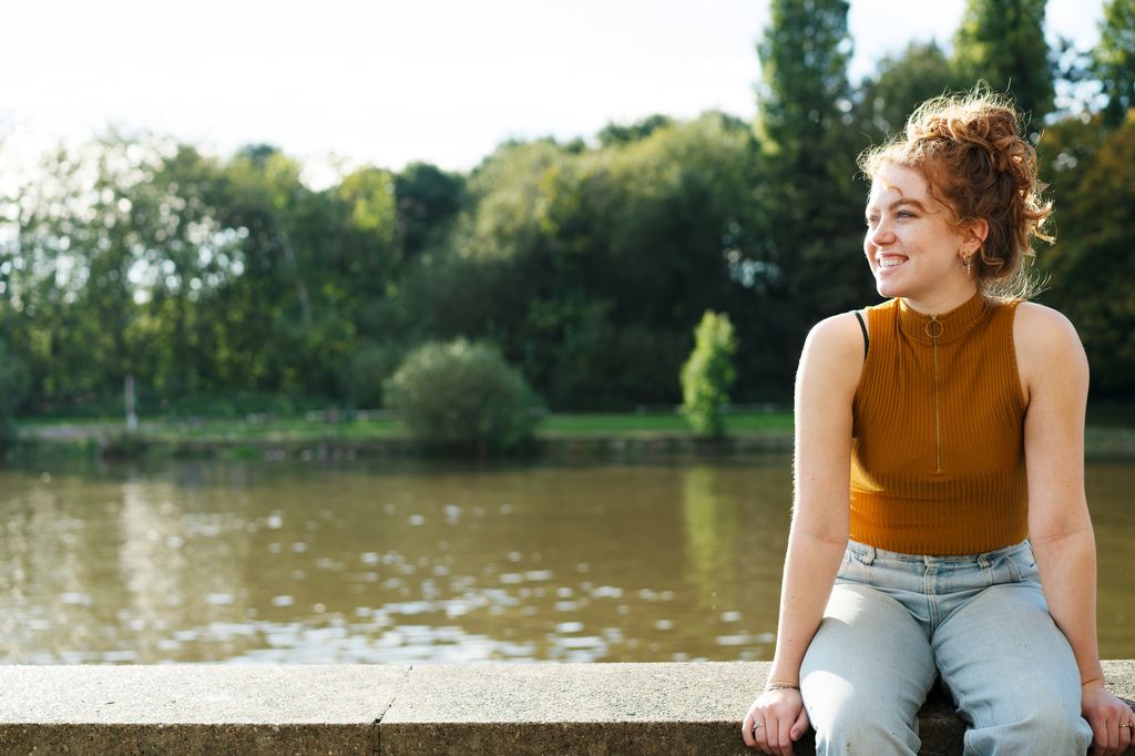 Woman sat on wall next to river, smiling