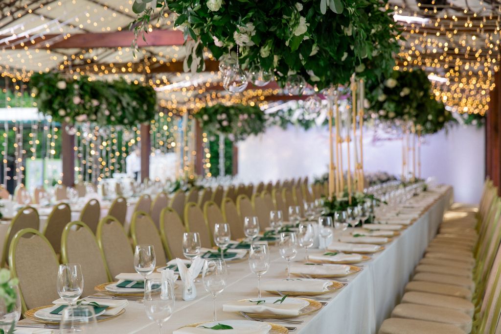 Lush floral garland with white roses hangs over the stylishly served white tables on the spacious terrace.