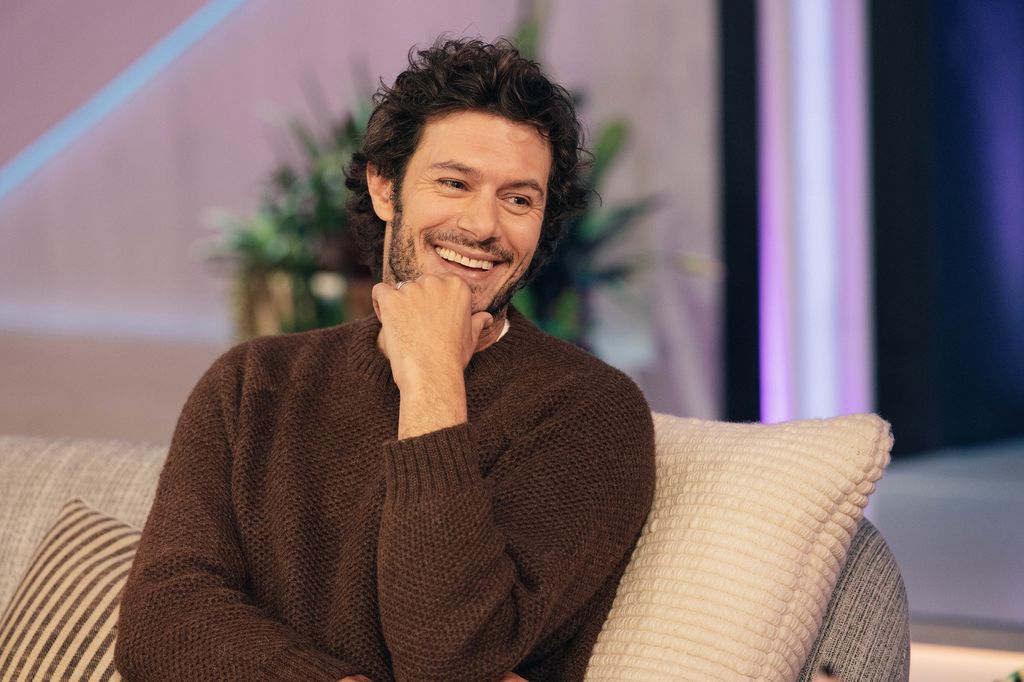 Adam Brody laughing and smiling in a brown jumper