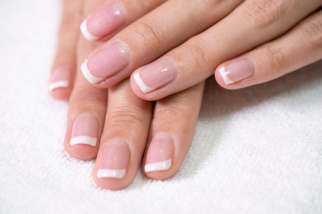 Closeup of nicely manicured female fingernails. One hand is placed on top of other, both on a white towel.