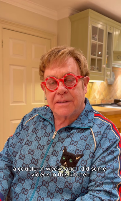 Sir Elton talking to camera in blue Gucci tracksuit