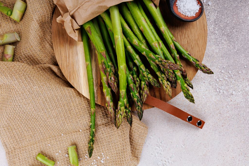 Top view of asparagus on cutting board in paper wrap with sea salt and neutral background