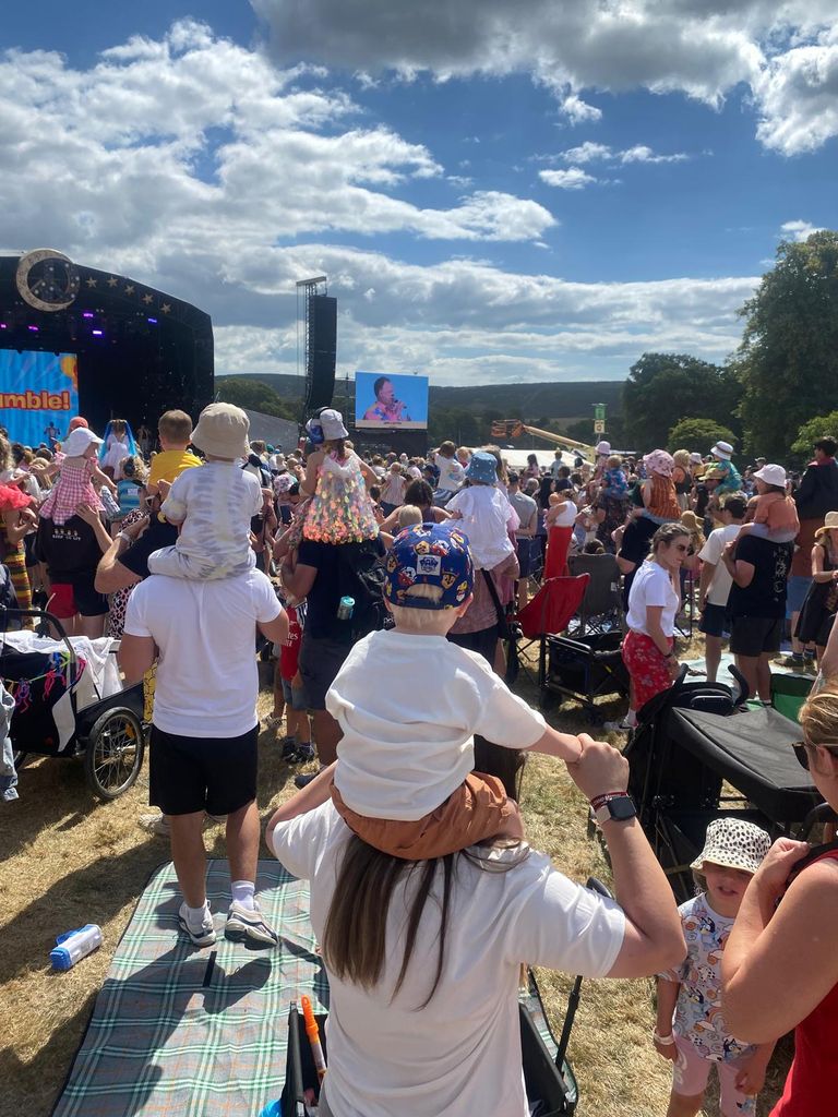 A crowd with children on shoulders in a field watching an act on a big stage