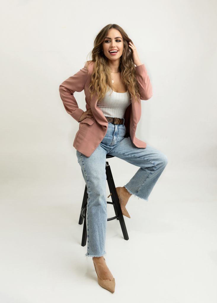 woman in blazer and jeans sitting on a stool