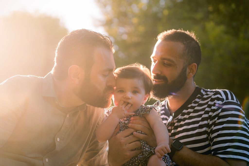 two fathers with daughter one kissing her on the head 