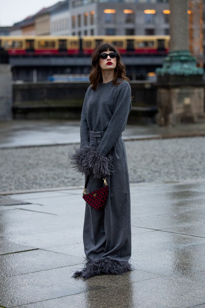 Lea Naumann wears full Prada look, grey jumper with feathers, wide leg pants with feathers, sunglasses, red bag on November 27, 2023 in Berlin,