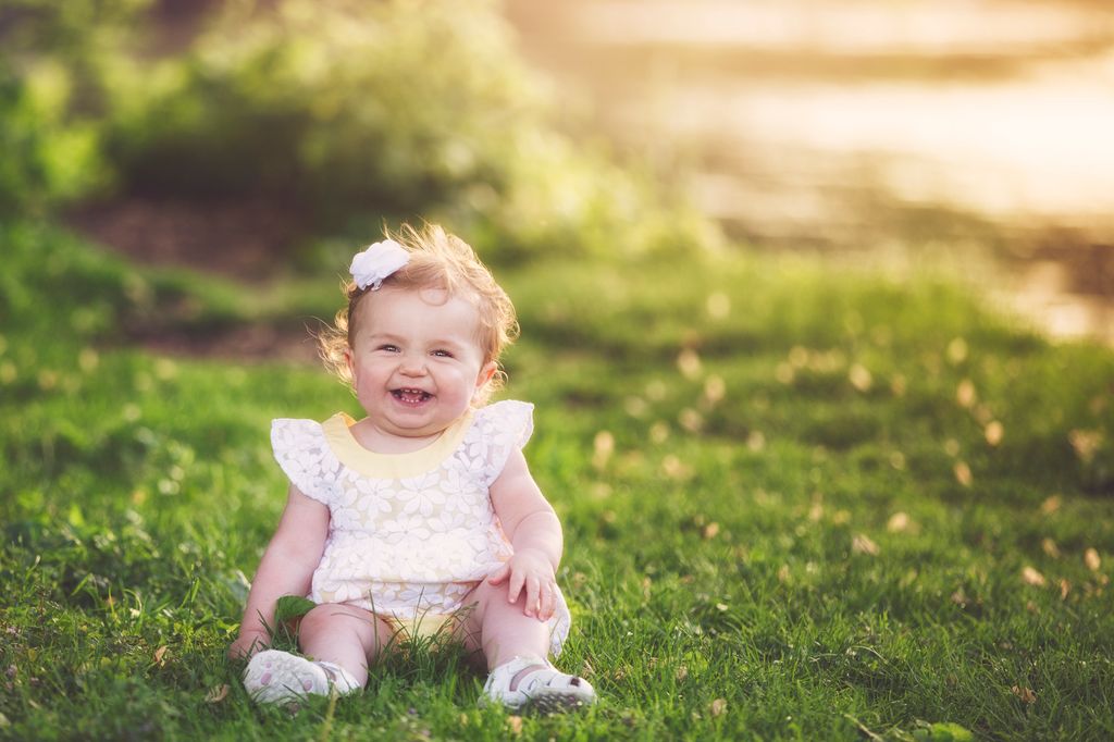 One year old baby girl seated on grass.