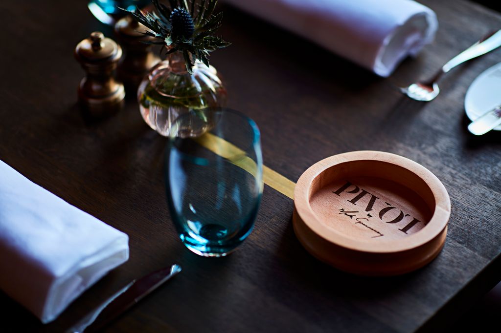 Close up of a table with a wooden bowl, cutlery, condiments and a glass