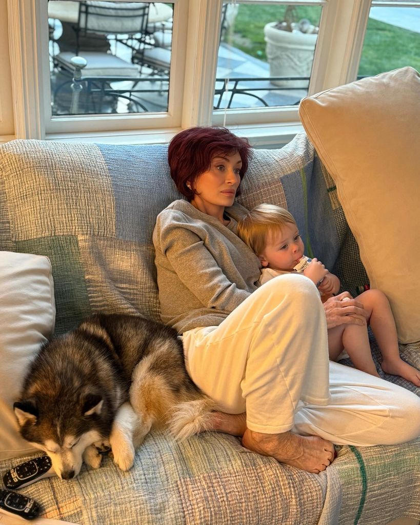 sharon osbourne sitting on sofa cuddling grandson sidney