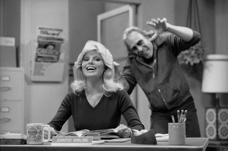 Dr. Johnny Fever (Howard Hesseman) clowns around behind Jennifer Marlowe's (Loni Anderson) back during a scene from WKRP in Cincinnati in 1978