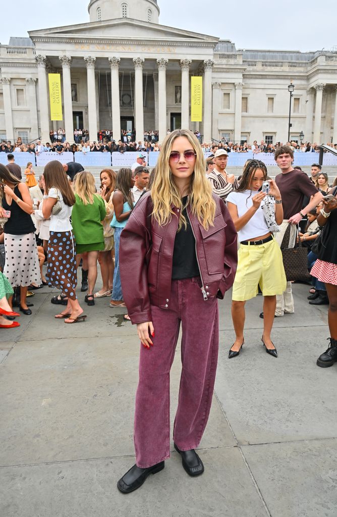 Cara Delevingne attends the Topshop & Topman AwW5 Show in Trafalgar Square. She wears a dark cranberyy coloured leather jacket and jeans with black shoes and sunglasses