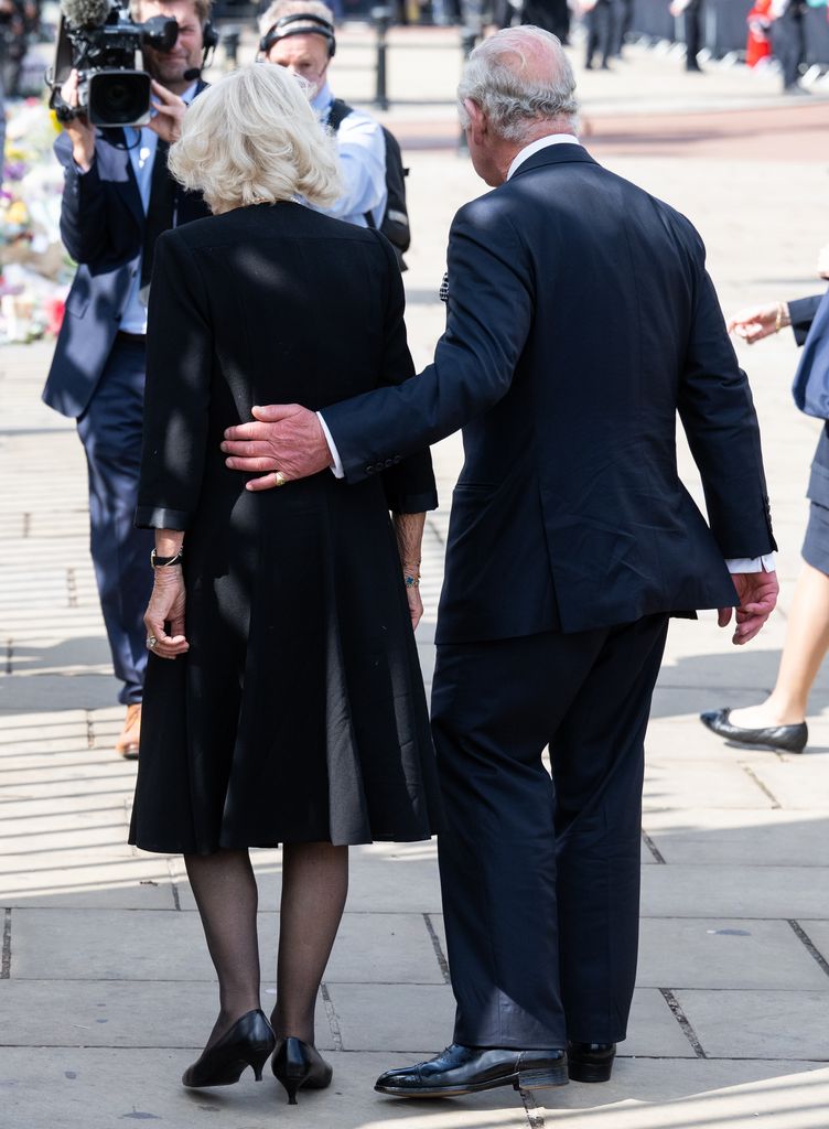 King Charles with an arm around Camilla while viewing floral tributes to the late Queen Elizabeth II outside Buckingham Palace